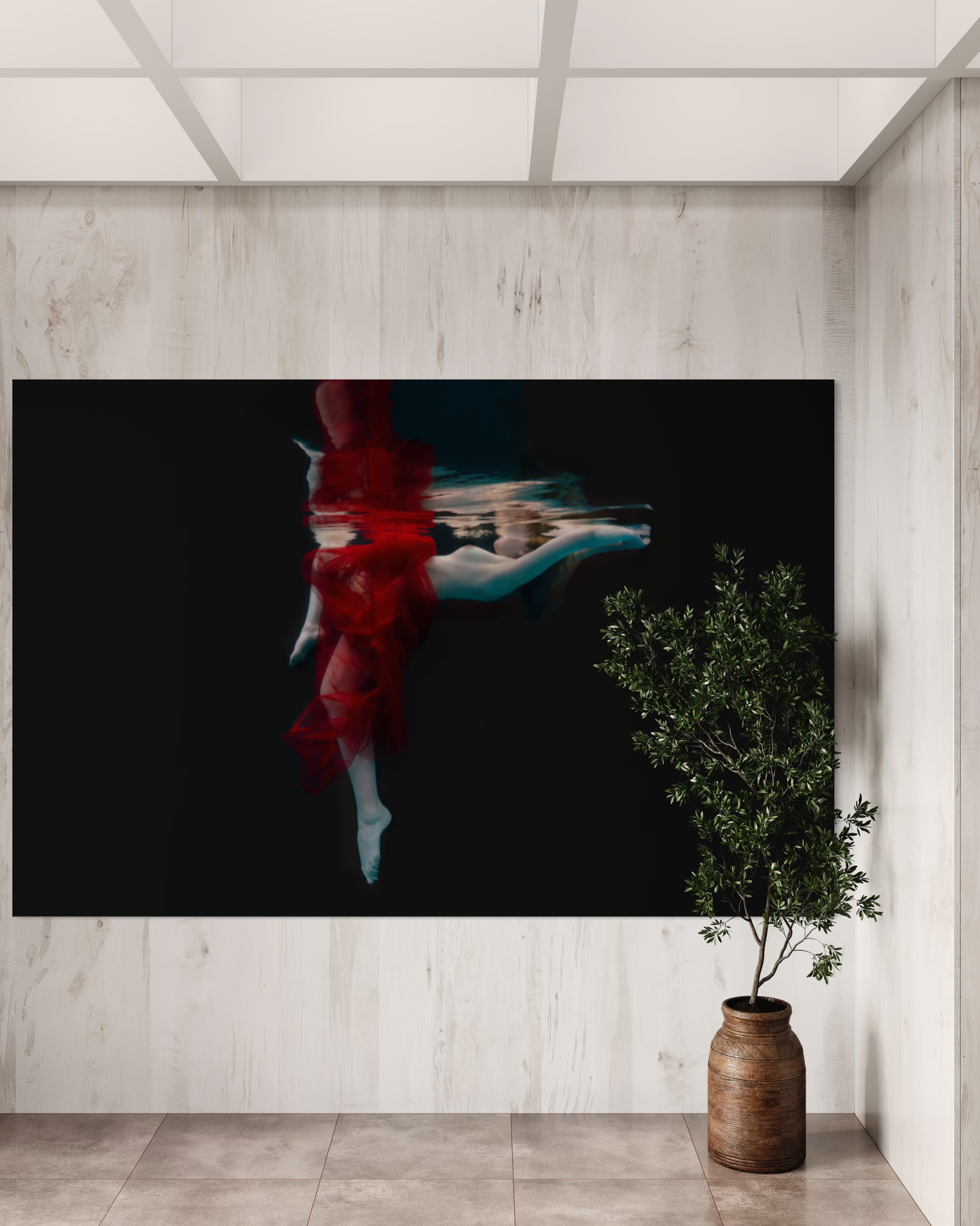 Within the depths of the sea, a stunning figure, wrapped in sheer red chiffon, floats gracefully amidst the aquatic realm. Her ethereal beauty and serene presence are accentuated by the play of light and shadow in the fine art photography. The mysterious allure of the underwater world surrounds her, evoking a sense of enchantment and tranquility