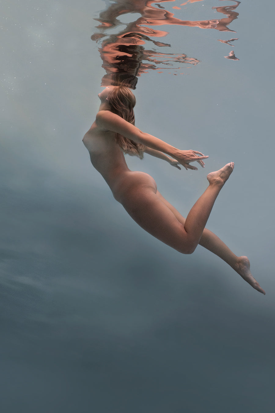 "Within the depths of the sea, a stunning figure, embodying the essence of a Naiad, floats gracefully amidst the aquatic realm. Her ethereal beauty and serene presence are accentuated by the play of light and shadow in the fine art photogray. The mysterious allure of the underwater world surrounds her, evoking a sense of enchantment and tranquility."