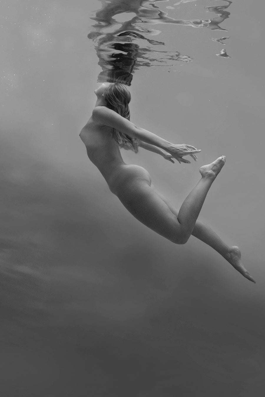 "Within the depths of the sea, a stunning figure, embodying the essence of a Naiad, floats gracefully amidst the aquatic realm. Her ethereal beauty and serene presence are accentuated by the play of light and shadow in the fine art photogray. The mysterious allure of the underwater world surrounds her, evoking a sense of enchantment and tranquility.